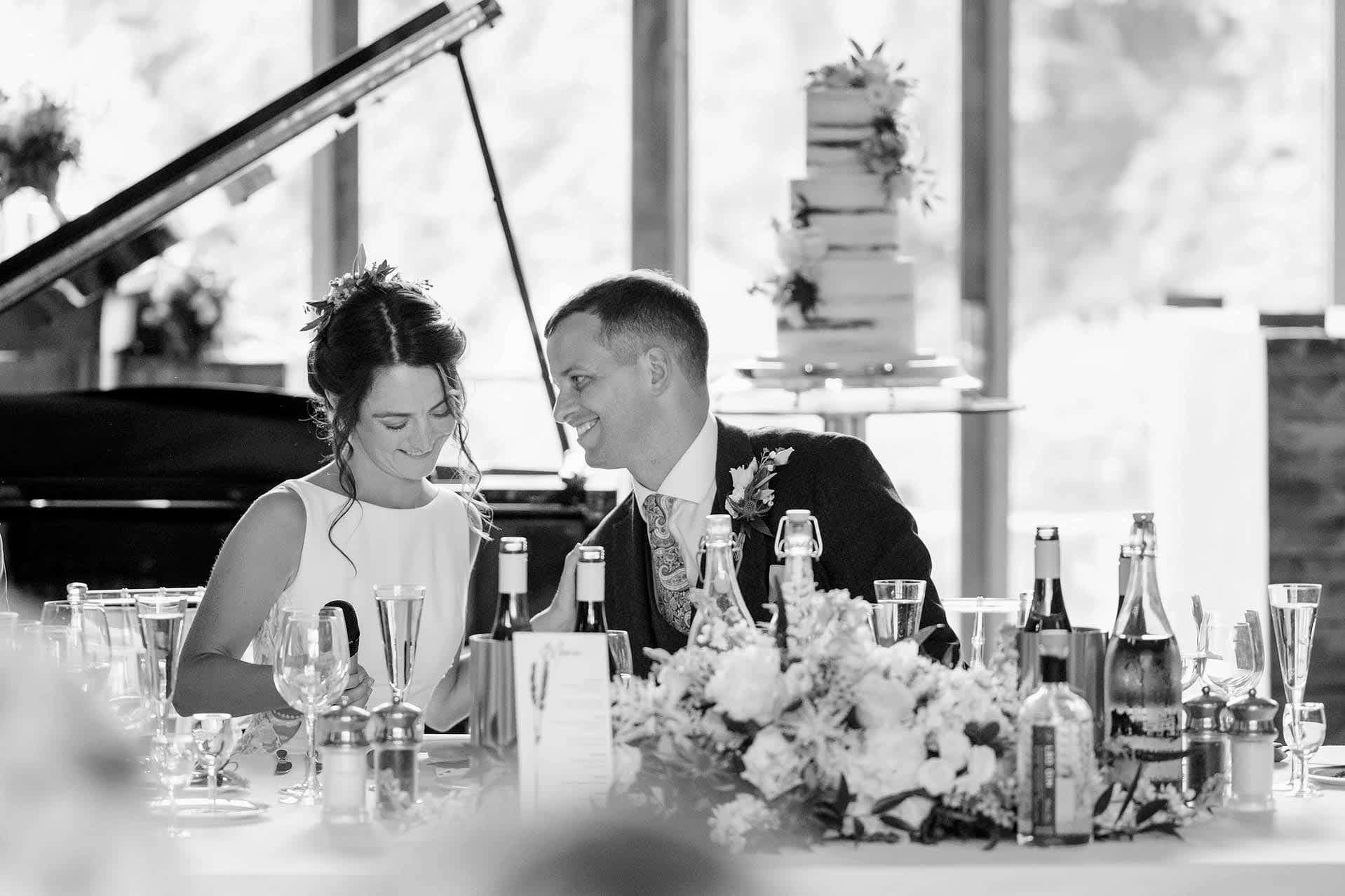 The bride and groom interacting with each other as the bride takes her seat after making a speech