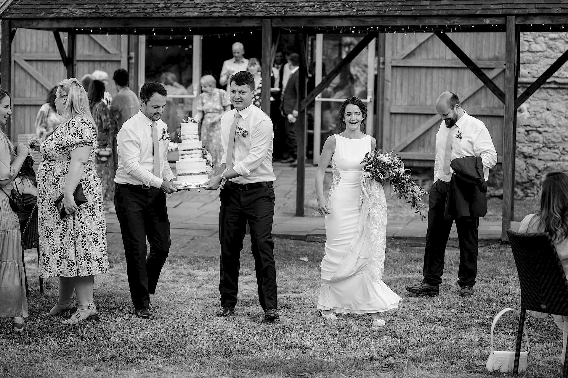 Two ushers carrying the wedding cake into the courtyard at Notley Abbey ready to be cut outside