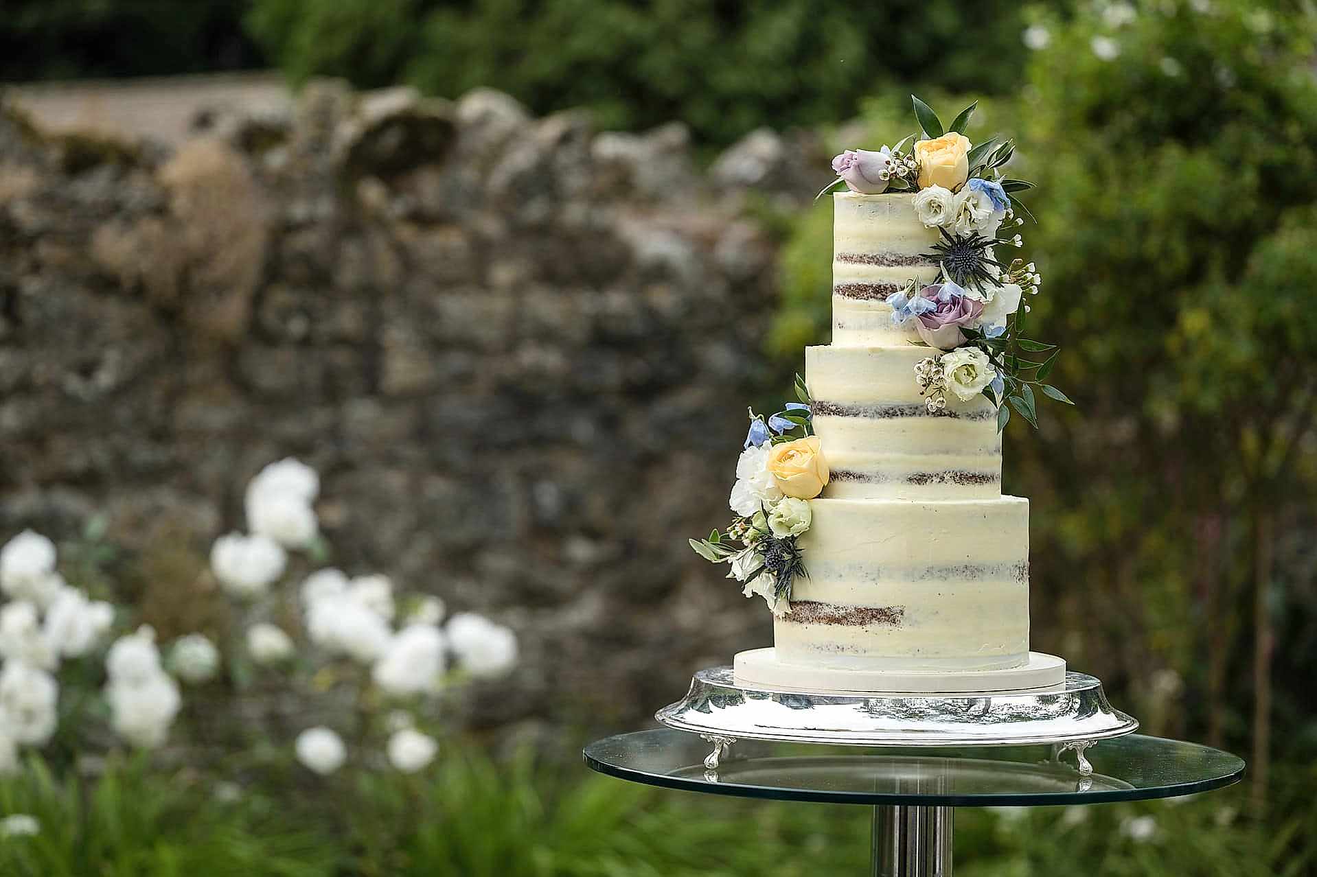 A semi naked wedding cake with fresh flowers displayed in the garden at Notley Abbey