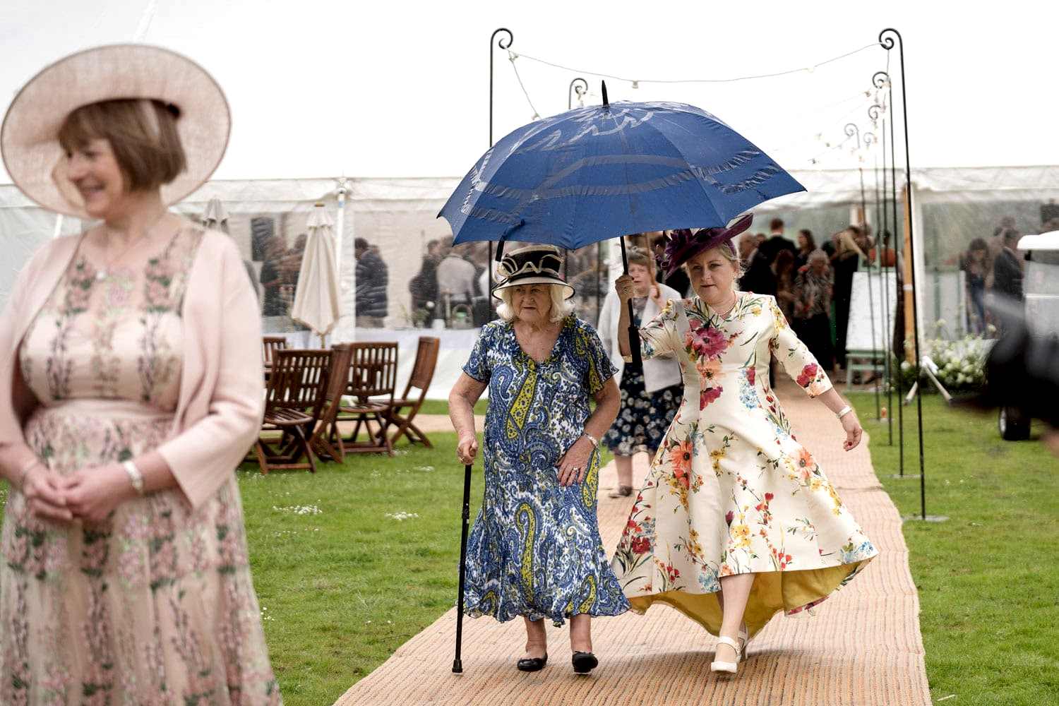 Wedding guests walking out of a marquee under umbrellas in the rain
